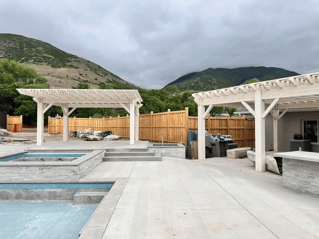 Patio Cover vs. Pergola Utah comparison featuring white pergolas, a poolside patio, and scenic mountain views. 